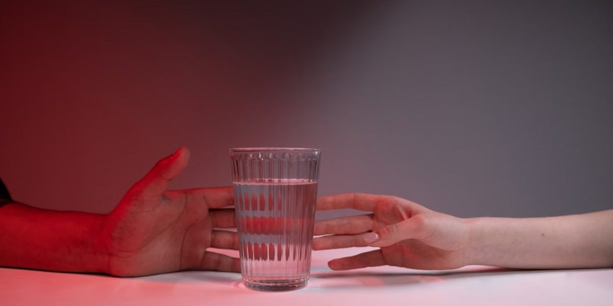 A striking image of two hands reaching for a glass of water on a red-lit background.