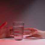 A striking image of two hands reaching for a glass of water on a red-lit background.