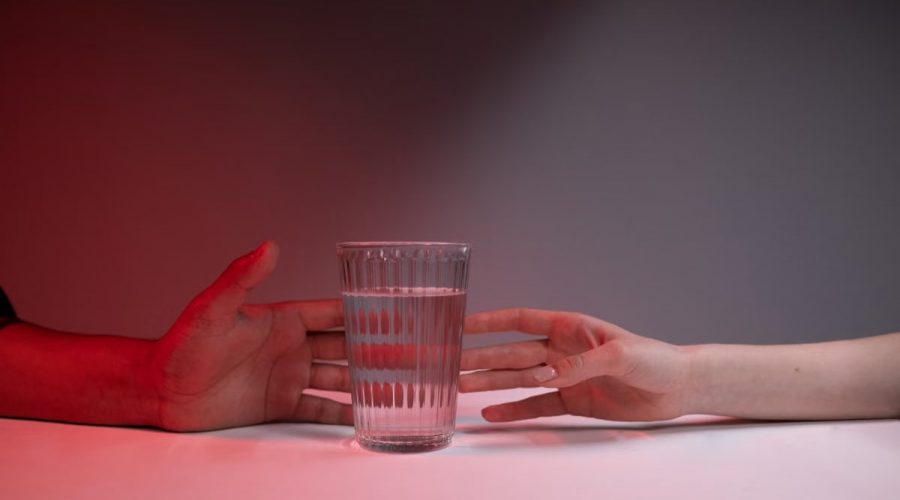 A striking image of two hands reaching for a glass of water on a red-lit background.